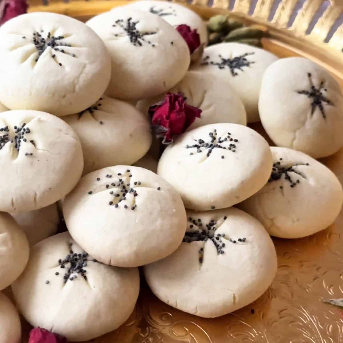 a close shot of nan e berenji cookies topped with poppy seeds and served on a copper tray with rose petals