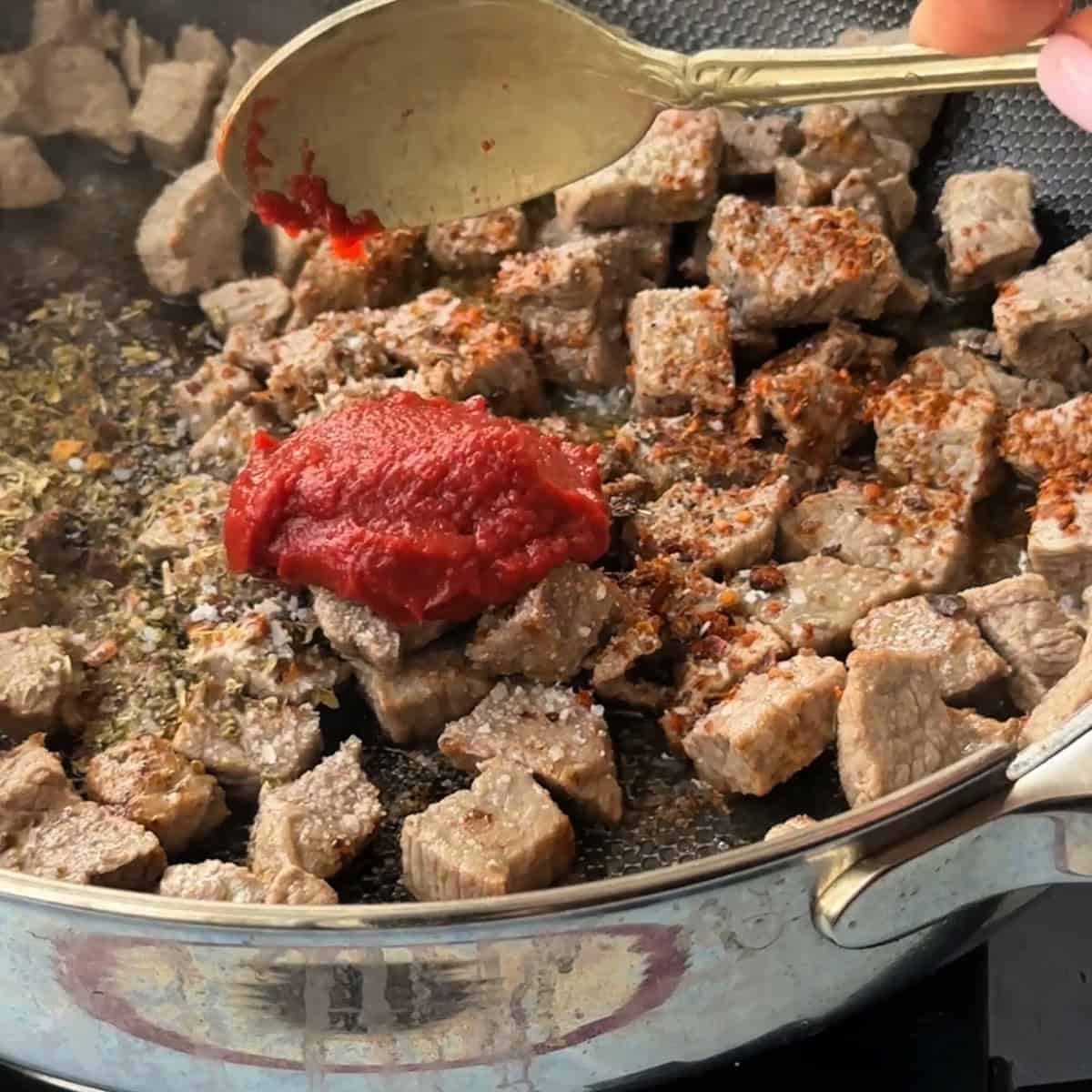 adding tomato paste to the beef cubes