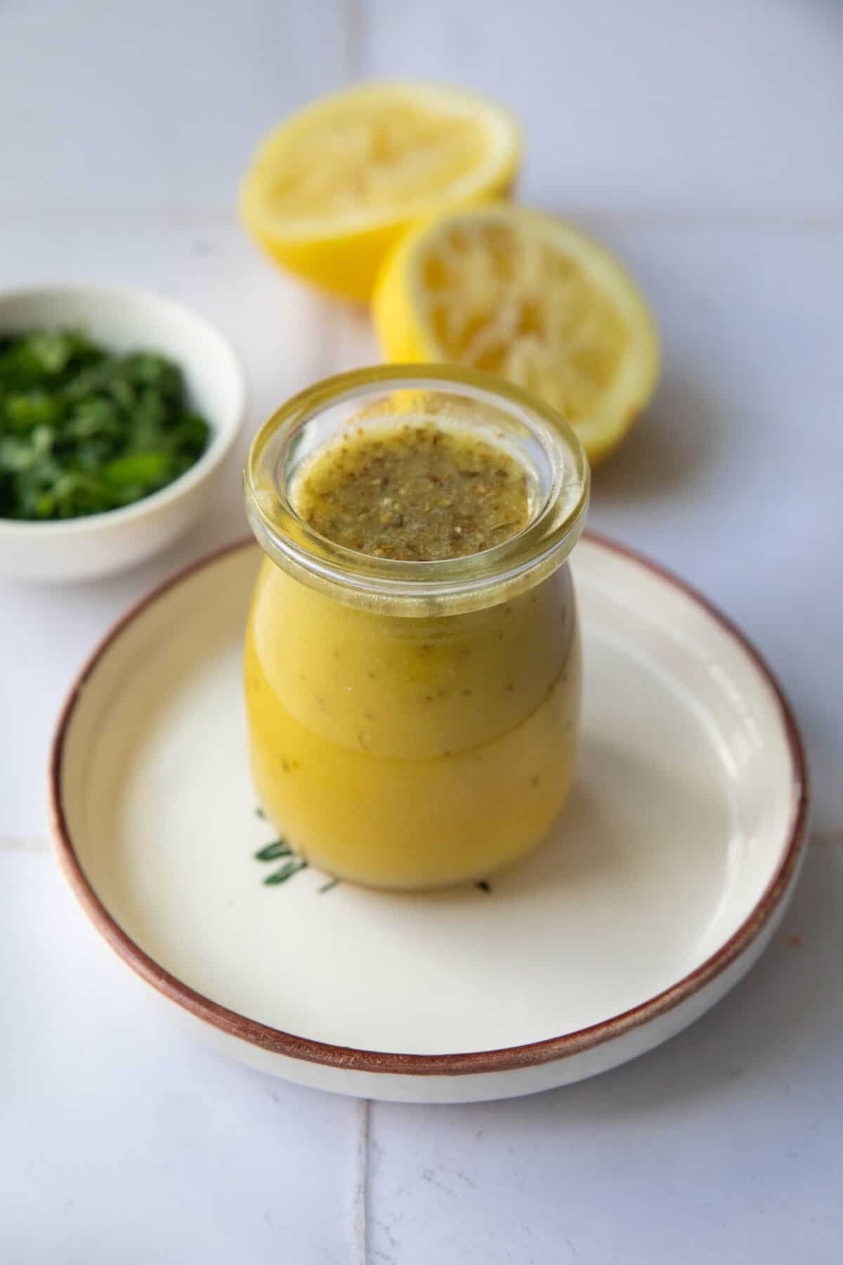 Mediterranean Salad Dressing a shot of a mason jar with Mediterranean salad dressing placed on a plate next to two halved lemons