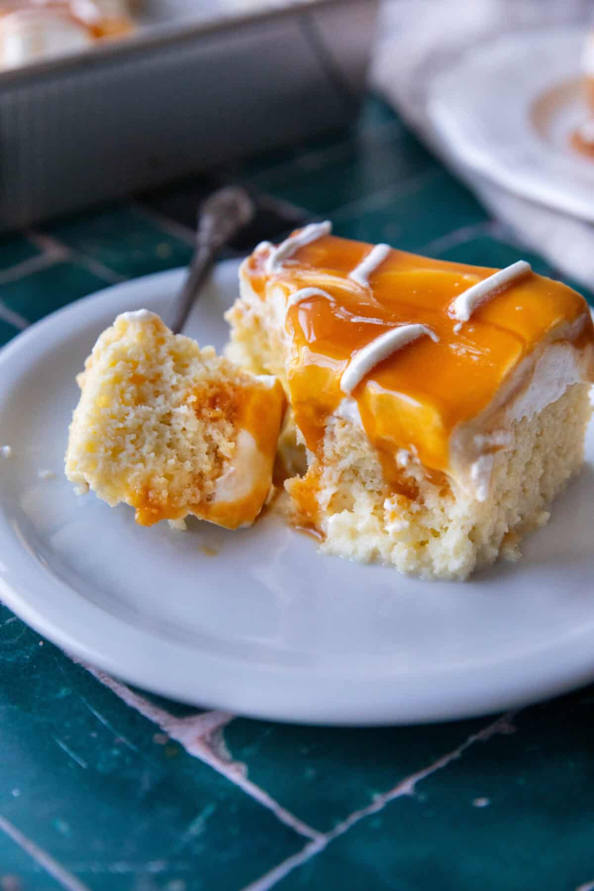 Turkish Milk Cake with Whipped Cream Moist piece of Trilece cake on a white plate with golden caramel sauce cut with a fork