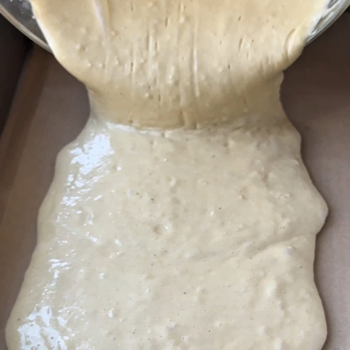 pouring the cake batter into a pan lined with parchment paper