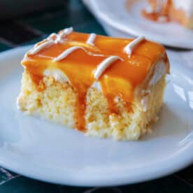 A square piece of Trilece, Turkish milk cake, topped with caramel sauce, served on a white plate.