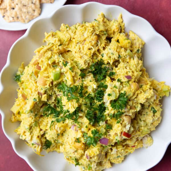 A bowl of chicken chickpea salad on a maroon backdrop.