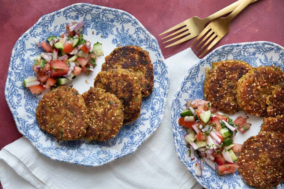 Two plates of lentil fritters on a maroon background. 