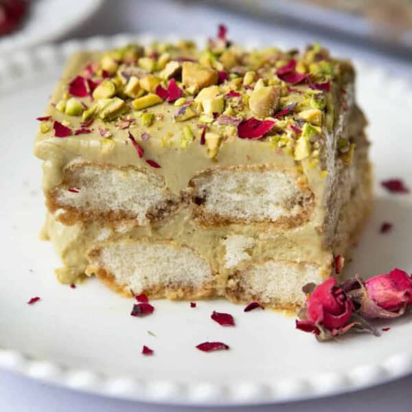 close up shot of pistachio tiramisu on a white plate decorated with pistachio and roses.