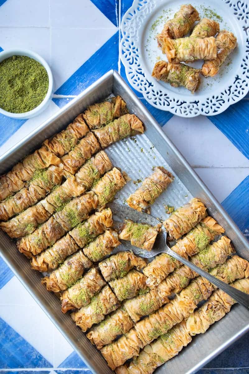 A pan of Burma baklava and a plate of rolled baklava on a blue and white background.
