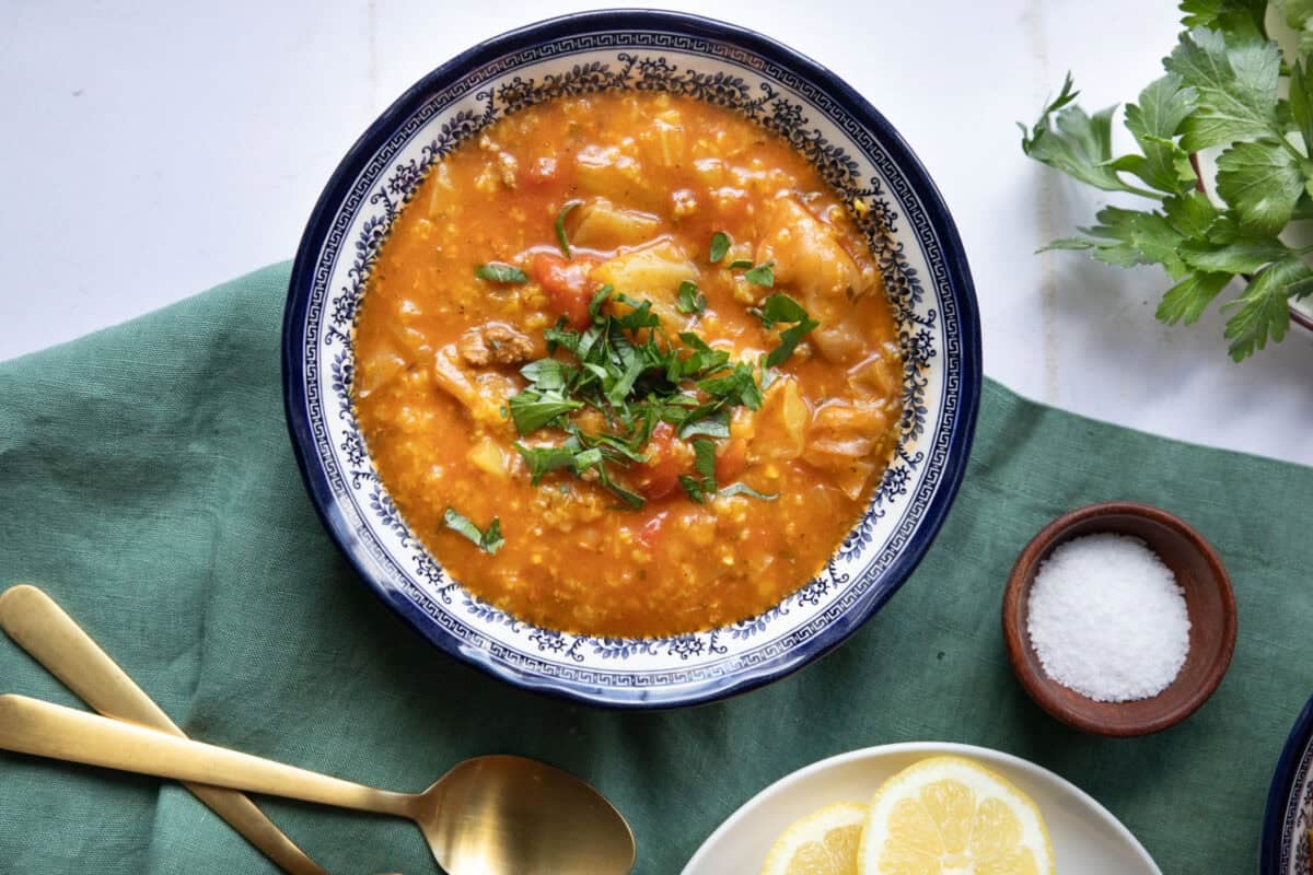A bowl of unstuffed cabbage soup in a blue bowl on a white background
