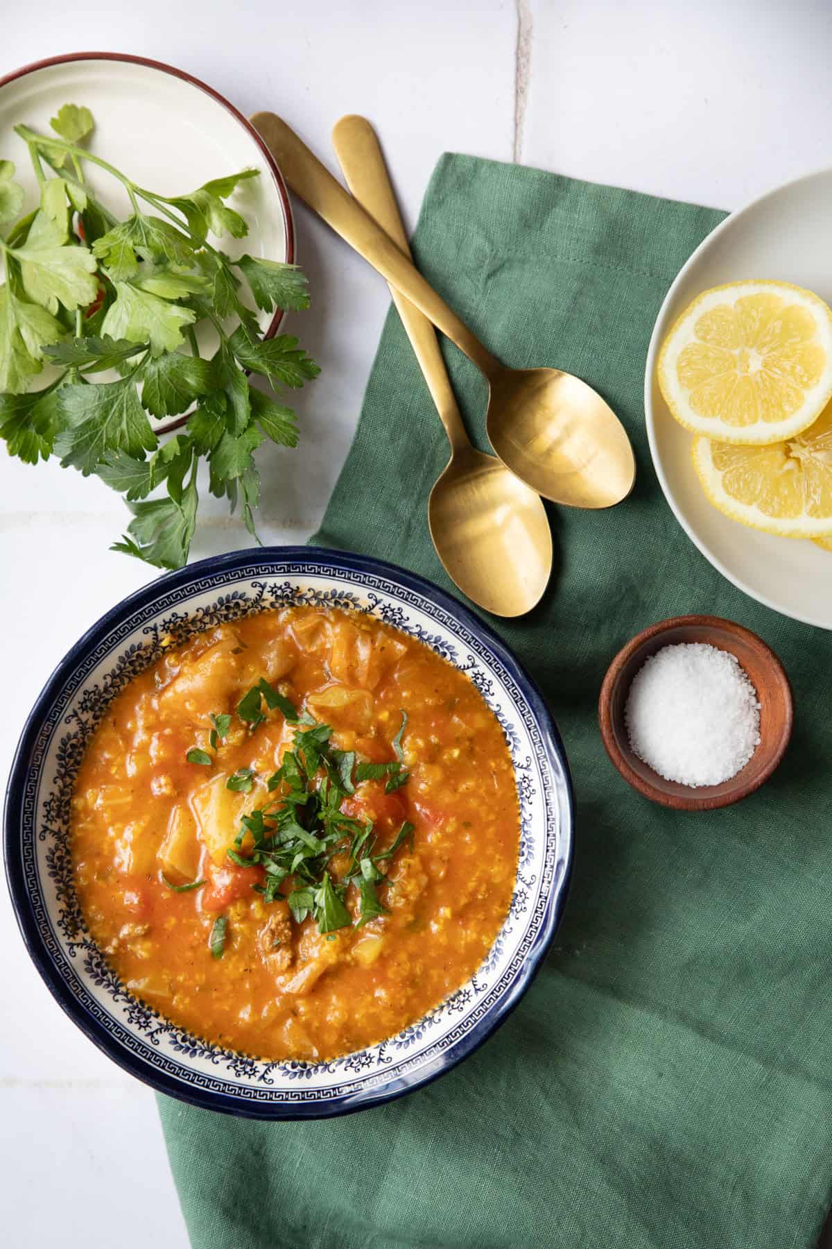 A bowl of unstuffed cabbage soup on a white background with a green linen and two spoons.