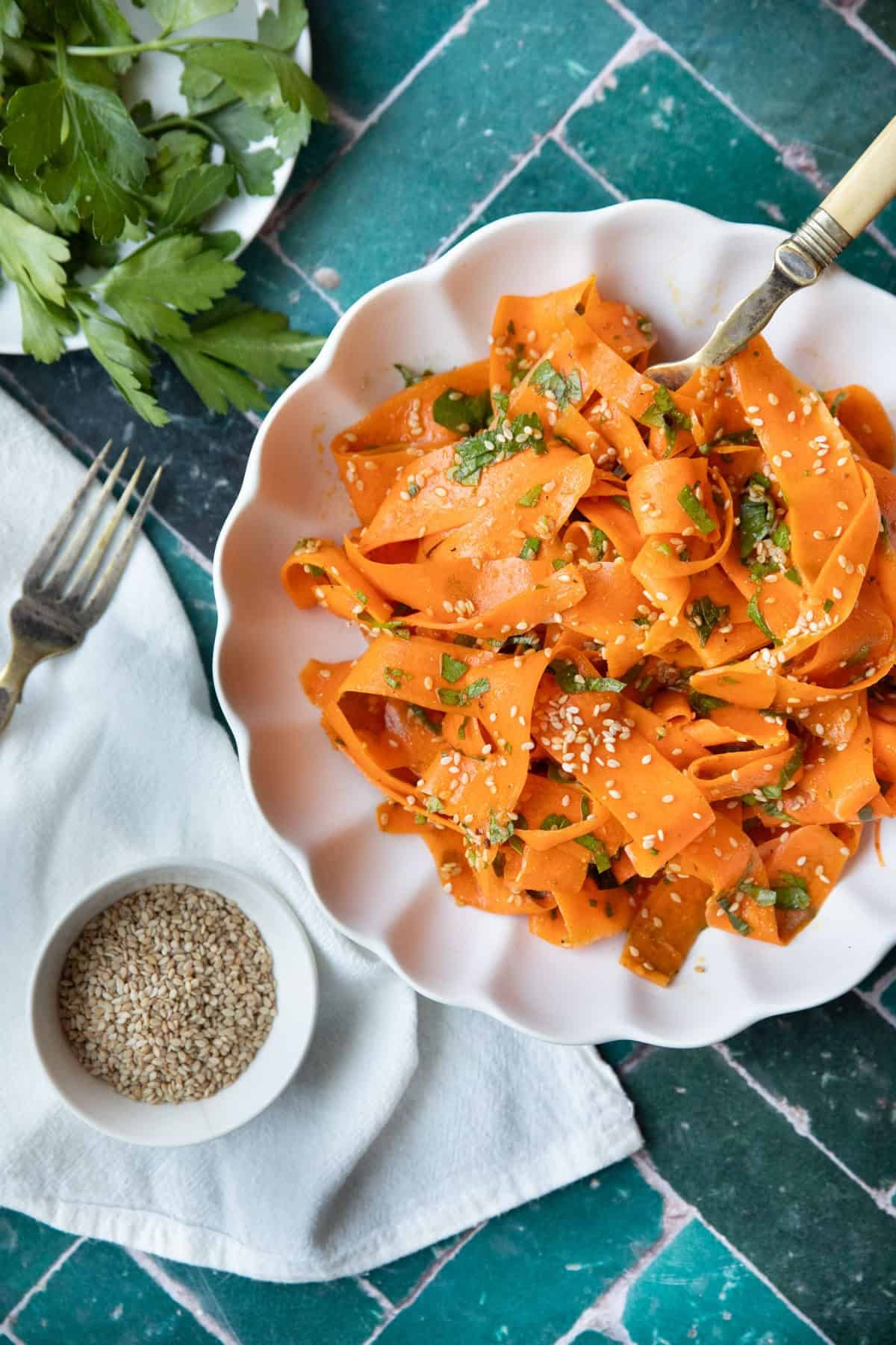 Carrot salad in a bowl on a green tile backdrop,