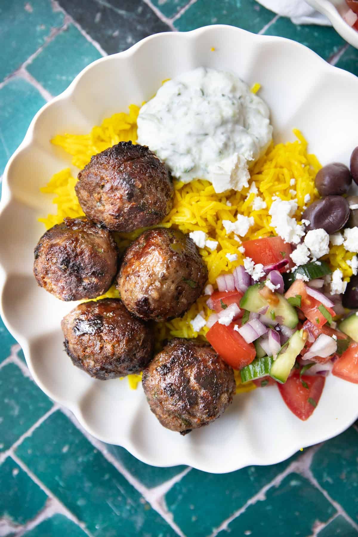 A bowl of lamb meatballs with yellow rice with salad and yogurt.
