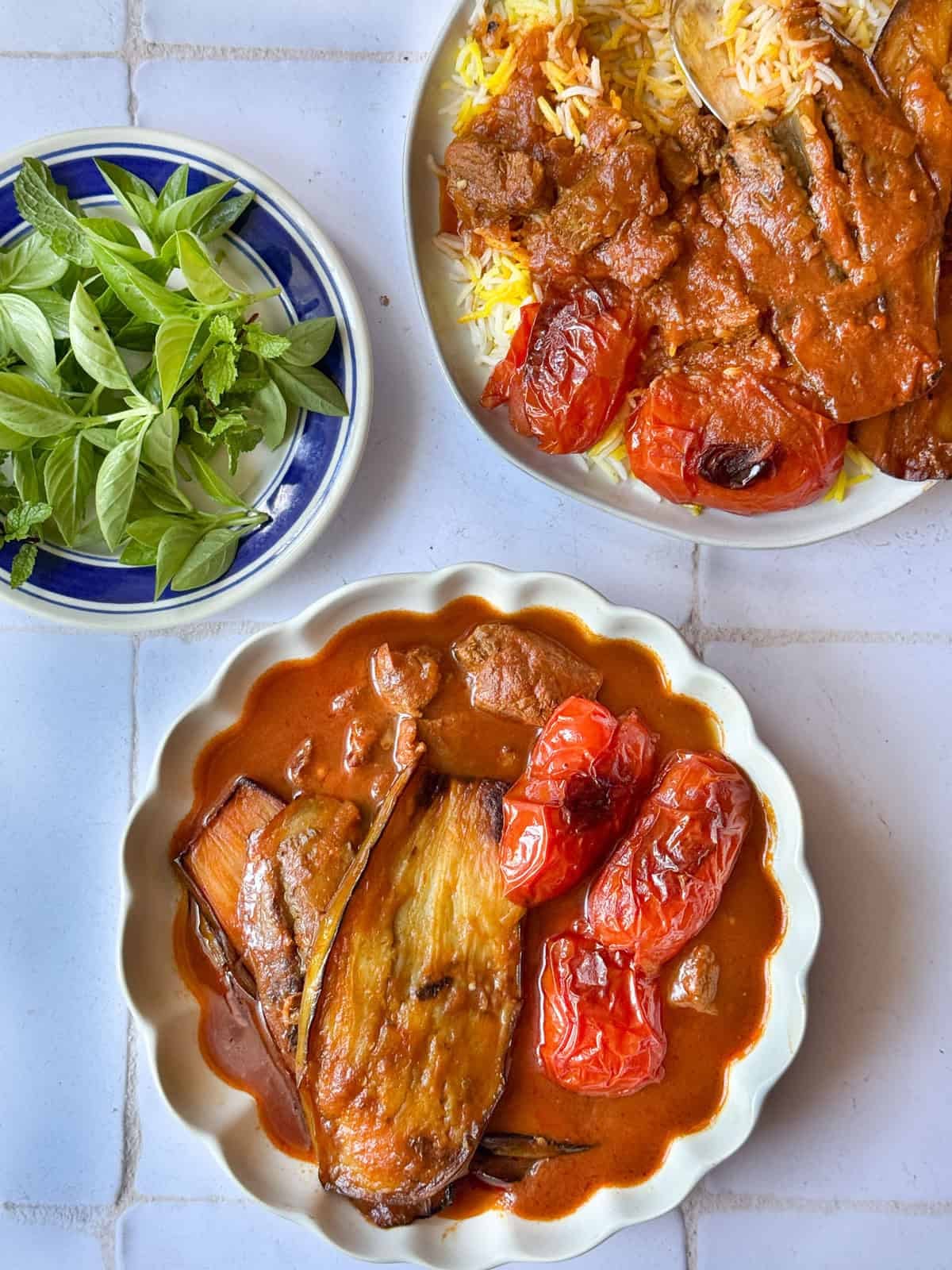 khoresh bademjan persian eggplant stew in a bowl with a plate of rice and stew on top and a plate of herbs.