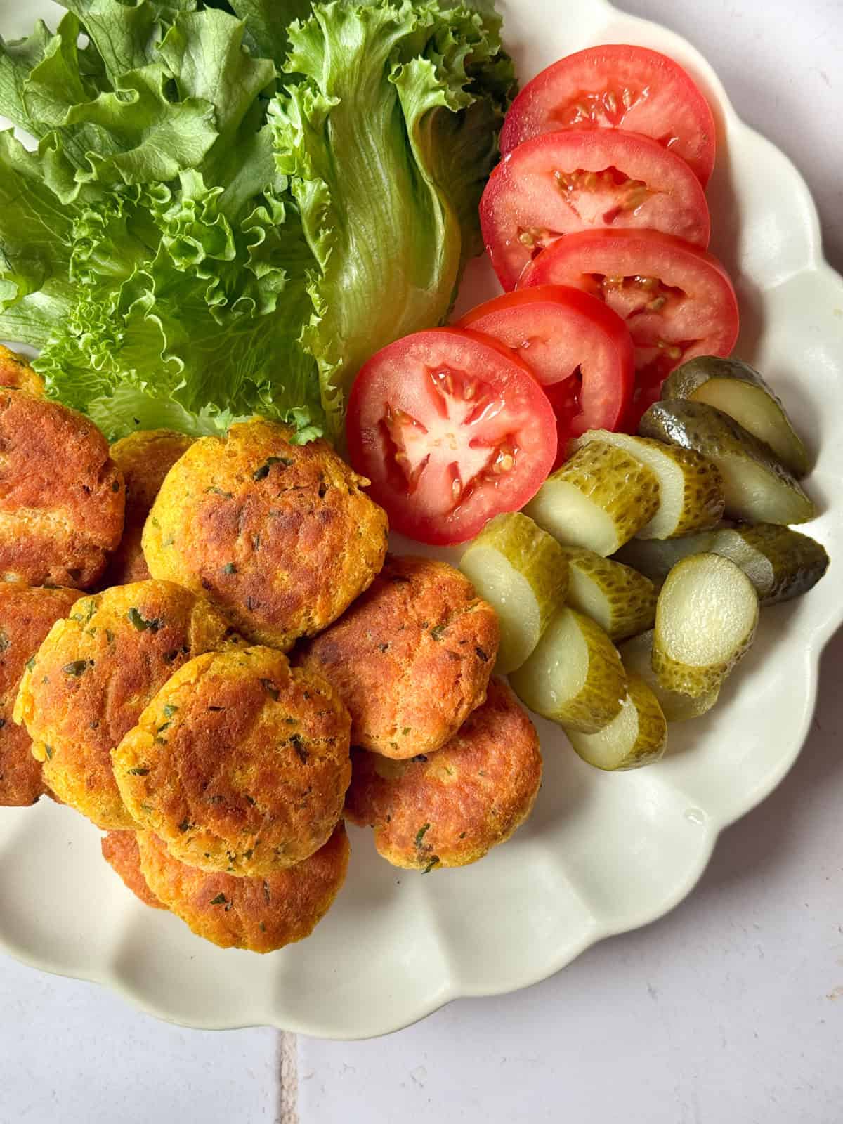 A plate of potato chicken patties with tomatoes, pickles and lettuce 