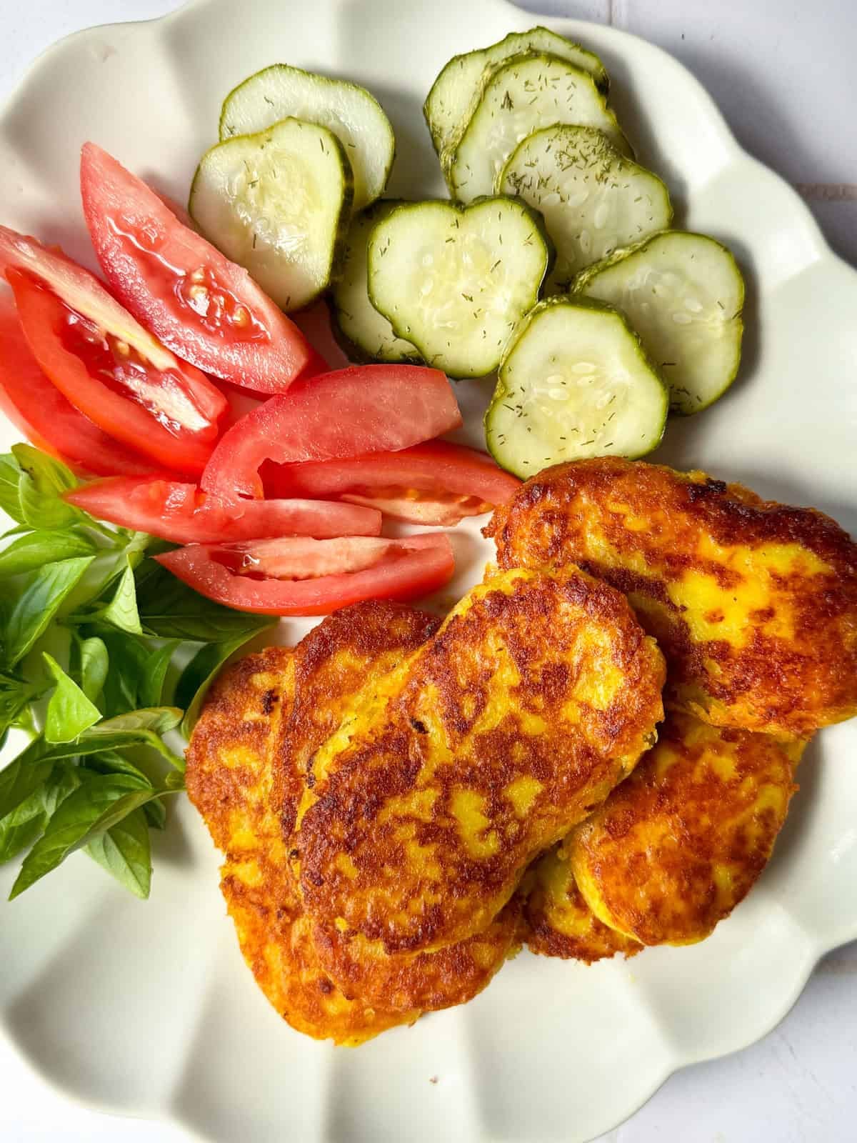 Persian potato patties in a plate with tomatoes herbs and pickles.